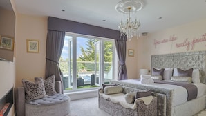 Une chambre avec un grand lit, un lustre, une cheminée et une vue sur l’extérieur.