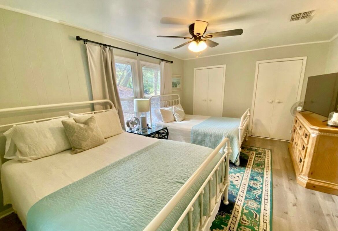 A bedroom with two beds, a ceiling fan, a dresser, and a window with curtains.