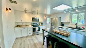 Una cocina moderna con gabinetes blancos, electrodomésticos de acero inoxidable, una isla central con taburetes y un tragaluz.