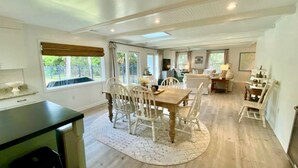 Un comedor amplio con una mesa de madera y sillas blancas, rodeado de grandes ventanales que ofrecen vistas al follaje.