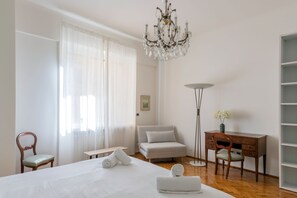 Une chambre d’hôtel avec un grand lit, un bureau, une chaise, une lampe sur pied et un lustre.