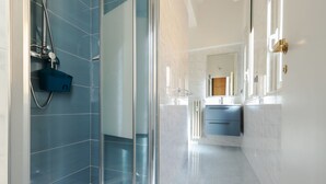 A modern bathroom with a glass shower enclosure, a blue sink, and a mirror with a gold frame. - JOIVY Charming 2BR flat near the Duomo (Milan)