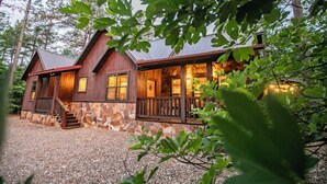 A rustic cabin with a stone facade, wooden porch, and a gravel driveway. - River Song- 1BR-Timber Creek Trails-Creekside (broken bow)