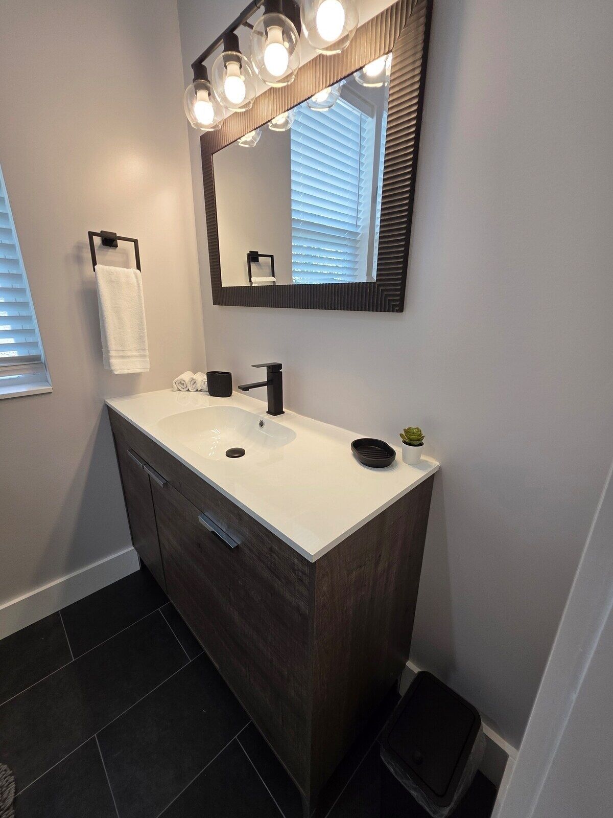 Un baño moderno con tocador blanco, mueble de madera oscura y un espejo grande iluminado.