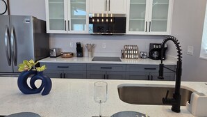 Una cocina moderna con armarios blancos, un refrigerador de acero inoxidable, una cafetera negra y una lámpara de techo original sobre la encimera.