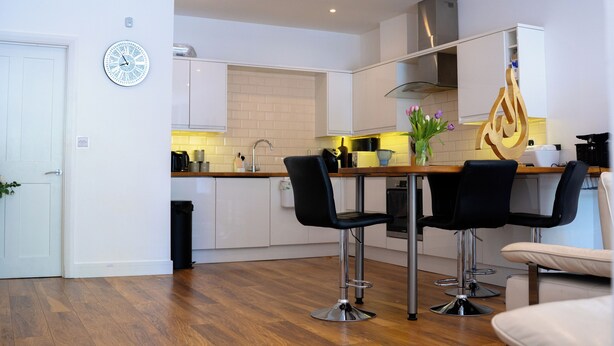 A modern kitchen with white cabinets, a wooden countertop, and a black chair.