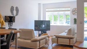 A modern living room with a sofa, a TV, and a dining area with a table and chairs.