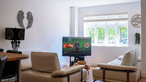 A living room with a television, two sofas, a dining table, and a window with blinds.