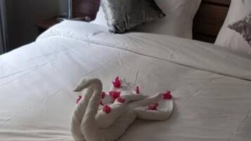 Una cama bien hecha con una toalla con forma de cisne y flores rosadas.