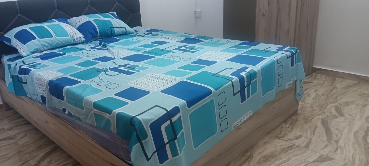 Ein Bett mit einem gemusterten Überwurf und Kissen, ein Holz-Kopfteil und ein Marmorboden.