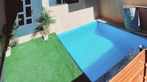 A modern two-story building with a swimming pool, a small garden, and a door with a window.