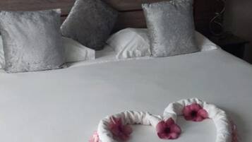 Een net opgemaakt bed met een bloemstuk in hartvorm in het midden, een houten hoofdbord en een muur met vier ingelijste schilderijen van tropische stranden.