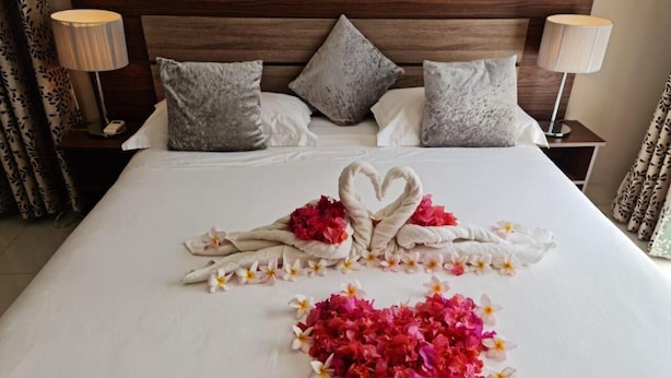 A neatly made bed with a heart-shaped towel arrangement and scattered flowers on the bed.