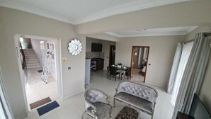 A living room with a sofa, armchair, and ottoman, a dining area with a table and chairs, and a kitchen in the background.
