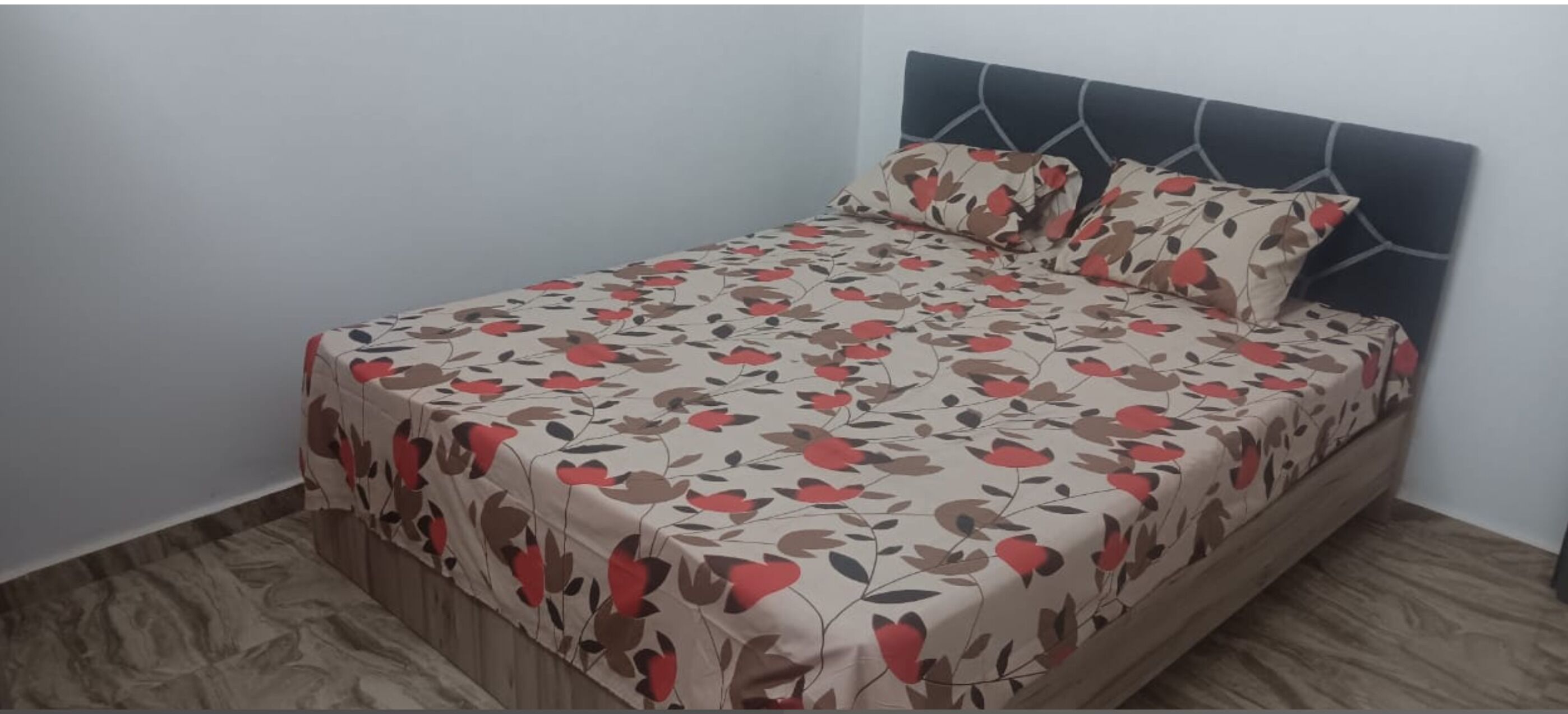 A single bed with a floral bedspread and matching pillows, a dark headboard, and a wooden floor.