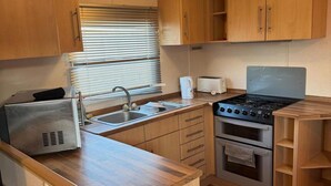 Una cocina compacta con fregadero, estufa y horno, armarios de madera y una ventana con persianas.