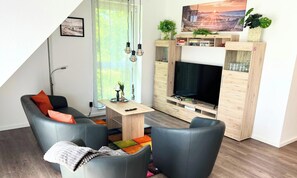 Un salon moderne avec un canapé, une table basse, un téléviseur et une bibliothèque.