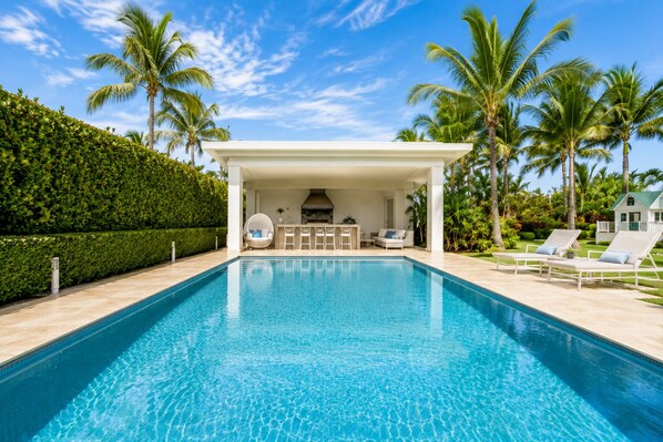 A swimming pool with lounge chairs and a covered seating area.