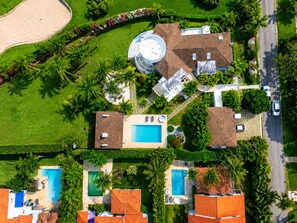 Vue aérienne d’un quartier résidentiel avec plusieurs maisons, une piscine et une structure circulaire surmontée d’une antenne parabolique.