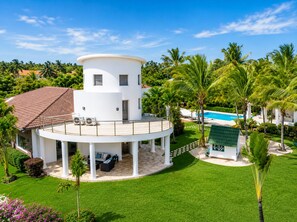 A modern white building with a circular patio, a swimming pool, and lush greenery.