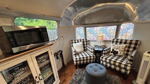 Ein kompaktes Wohnmobil-Interieur mit einer West Bend Mikrowelle, einer karierten Sofagarnitur, einem kleinen Tisch mit Lampe und einem Zierkissen.