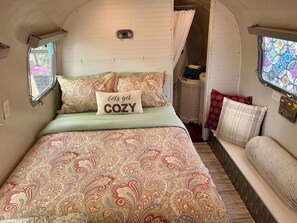 Un interior acogedor con una cama que incluye una almohada que dice 'let's get COZY', ropa de cama estampada y un ventanal con vistas.
