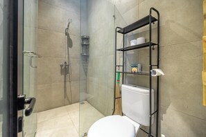 Een moderne badkamer met een douchecabine van glas, een toilet en een metalen plank met toiletartikelen.