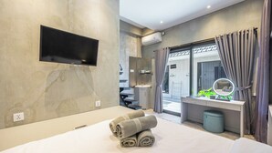 Ein modernes Hotelzimmer mit einem großen Bett, einem wandmontierten Flachbildfernseher, einem Schminktisch mit Spiegel und Blick ins Freie durch das Fenster.
