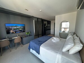 Moderni hotellihuone, jossa on sänky, työpöytä, tuoli, televisio ja näkymä kaupunkiin.