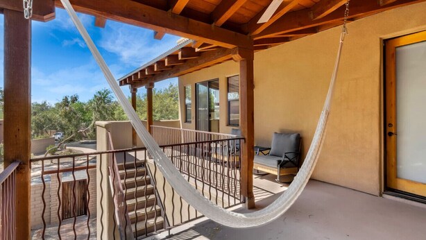 A hammock on a balcony with a view of a residential area and a door to the right.