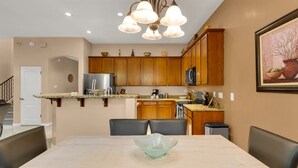 A modern kitchen with wooden cabinets, a stainless steel refrigerator, a microwave, and a granite countertop. There is a dining area with a marble table and black chairs.