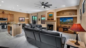 A modern living room with a large gray sectional sofa, a fireplace, and a dining area with a kitchen in the background.