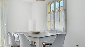 A dining area with a rectangular table, six white chairs with wooden legs, and a wooden bowl on the table.