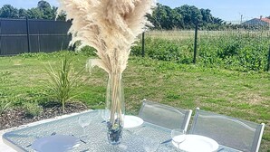 An outdoor dining table with a clear glass top, surrounded by metal chairs.