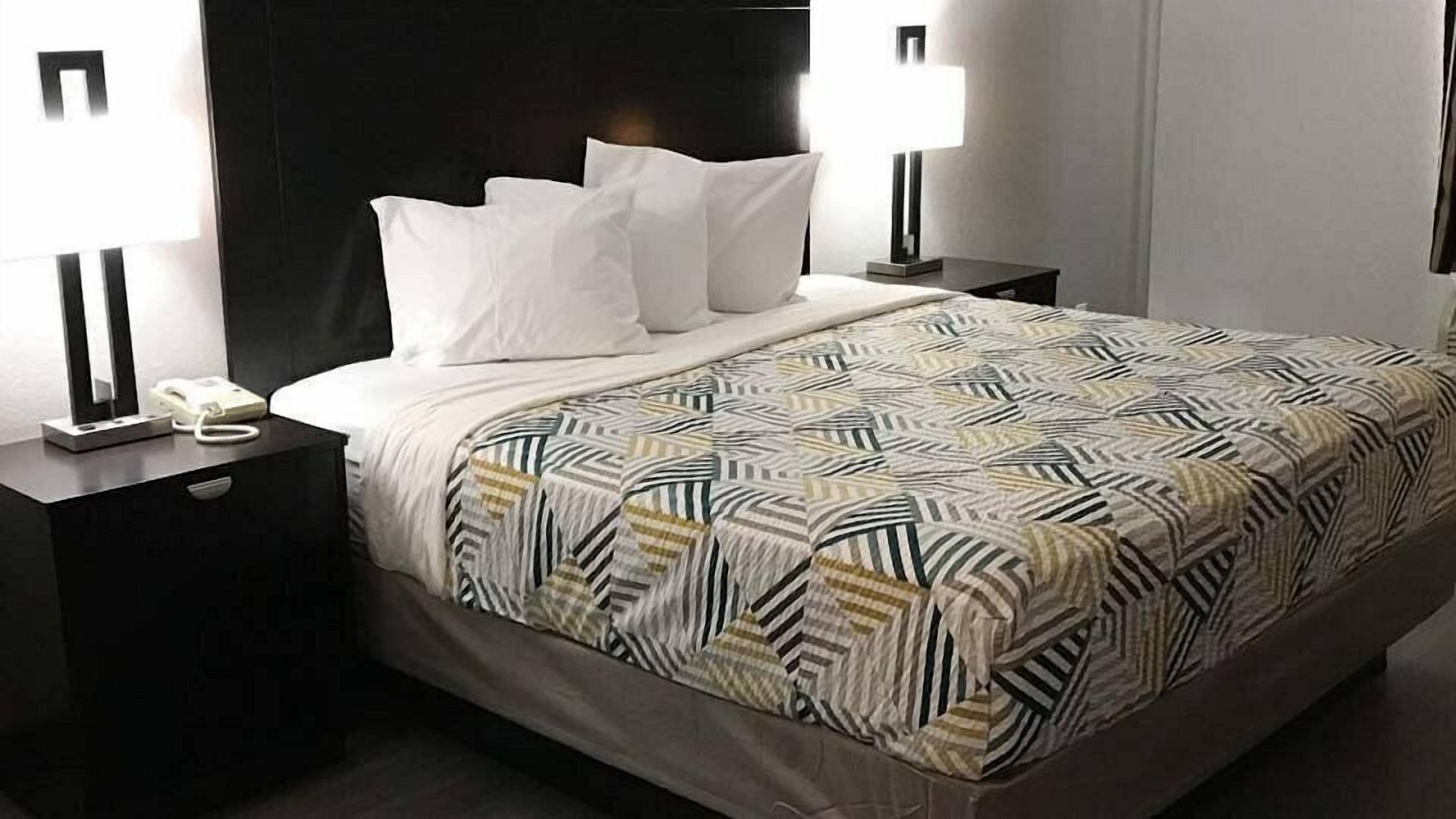 A neatly made bed with a patterned bedspread, two bedside lamps, and a bedside phone on a dark nightstand.