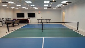 A tennis court with a net, a pool table, and chairs in a room with a white ceiling and walls. - Home Place Suites (Bartlesville)