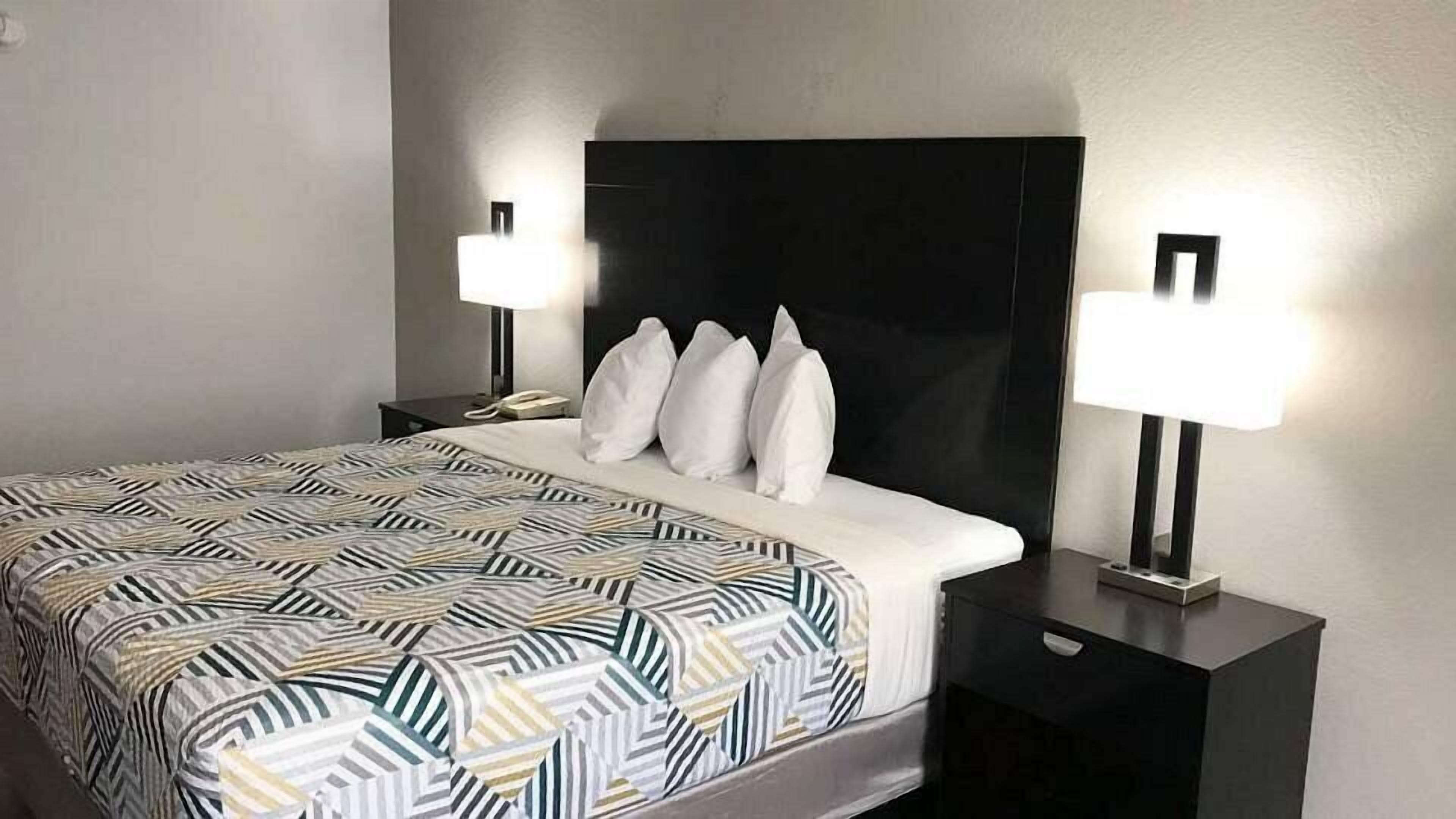 Une chambre d’hôtel avec un lit, deux tables de chevet, une tête de lit noire et deux lampes fixées au mur.