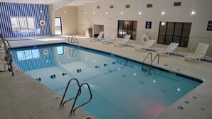 An indoor swimming pool with clear water, surrounded by lounge chairs and a tiled deck. - Home Place Suites (Bartlesville)