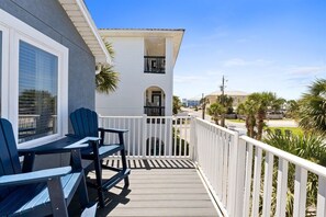 A balcony with two Adirondack chairs, a white railing, and a view of a building with a balcony.