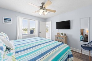 A bedroom with a bed, a ceiling fan, a television, a dresser, and a window with blinds.