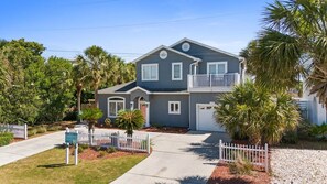 A two-story house with a balcony, surrounded by a white picket fence, palm trees, and a clear sky. - Hot Tub, Sleeps 10, 1 block to beach access, Pets (Panama City Beach)