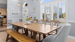 A dining room with a wooden table and benches, a chandelier, and a view through a window with shutters. - Hot Tub, Sleeps 10, 1 block to beach access, Pets (Panama City Beach)
