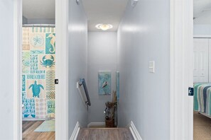 Un pasillo estrecho con piso de madera, una puerta blanca con cortina decorativa y un cuadro de un pájaro en la pared.