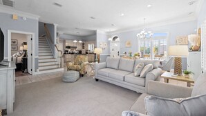 A spacious living room with a neutral color palette, a staircase leading to the upper floor, and a kitchen area visible in the background. - Hot Tub, Sleeps 10, 1 block to beach access, Pets (Panama City Beach)