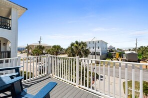 A balcony with a white railing, a blue bench, and a view of a street with buildings and palm trees. - Hot Tub, Sleeps 10, 1 block to beach access, Pets (Panama City Beach)