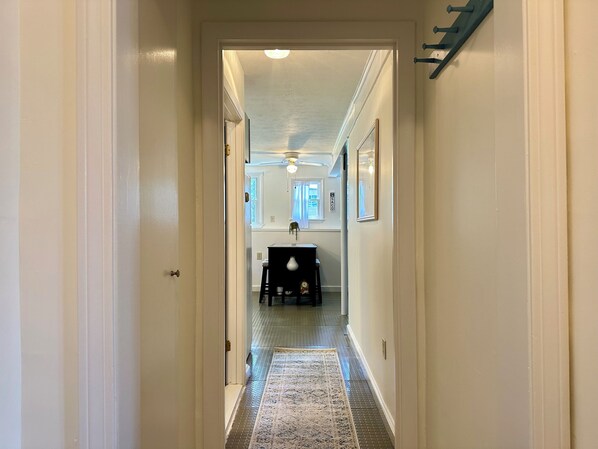 A hallway with a patterned rug, a dining area with a table and chairs, and a ceiling fan. - “Below Deck” at Ferry Beach - 2 bedroom apartment steps from the beach! (Saco)