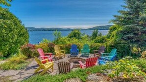 A lakeside view with colorful Adirondack chairs arranged around a fire pit. - Luxury Meets the Lake (Lake George)