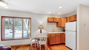 A compact kitchen with wooden cabinets, a white refrigerator, and a dining area with a table and chairs. - Luxury Meets the Lake (Lake George)
