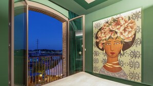 Et soveværelse med en stor seng, en balkon med udsigt over byen og et maleri på væggen.