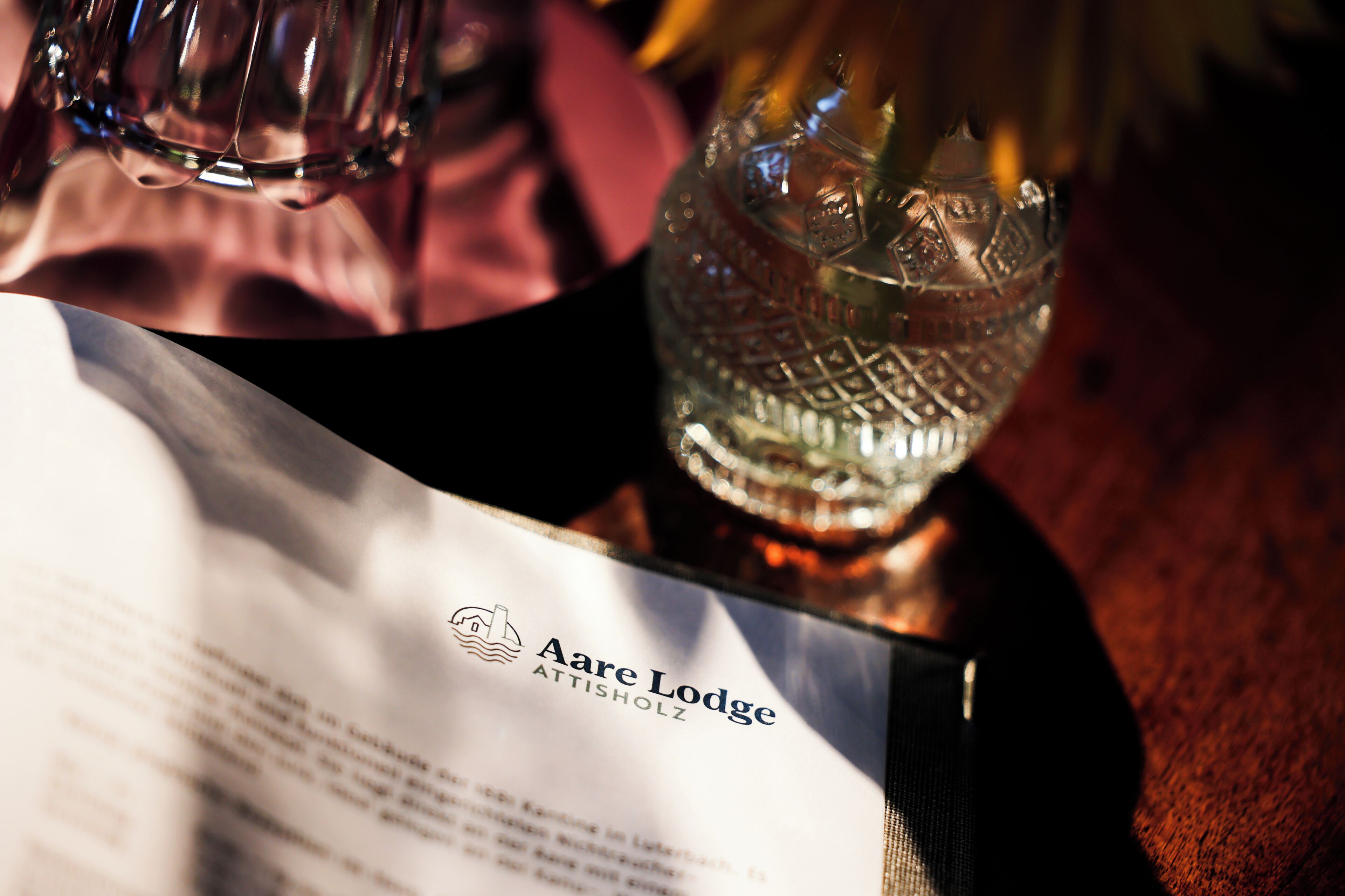 A menu with the logo 'Aare Lodge' and a glass with a floral arrangement.